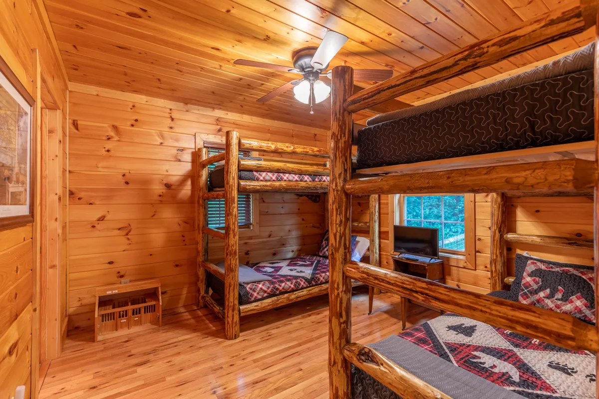This image showcases a cozy bunk room with two sets of twin-over-twin bunk beds surrounded by warm wooden paneling and soft textiles, evoking a sense of adventure and community, perfect for kids or group stays.
