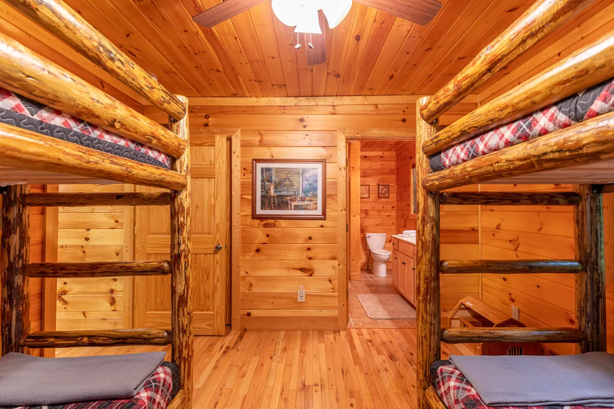 This image shows a bunk room with wooden paneling, featuring multiple bunk beds, framed artwork, and an entrance to a bathroom. The space is inviting, cozy, and clearly designed for children or singles, making it ideal for group accommodations. The layout encourages togetherness and fun, aligning with the shared spaces described in the section.