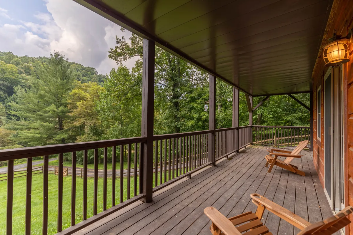 A spacious wooden deck with ample outdoor seating, framed by greenery and mountain views. The setting suggests a seamless flow from indoor living to outdoor adventure, perfect for gatherings, relaxation, or stargazing nights by the river.