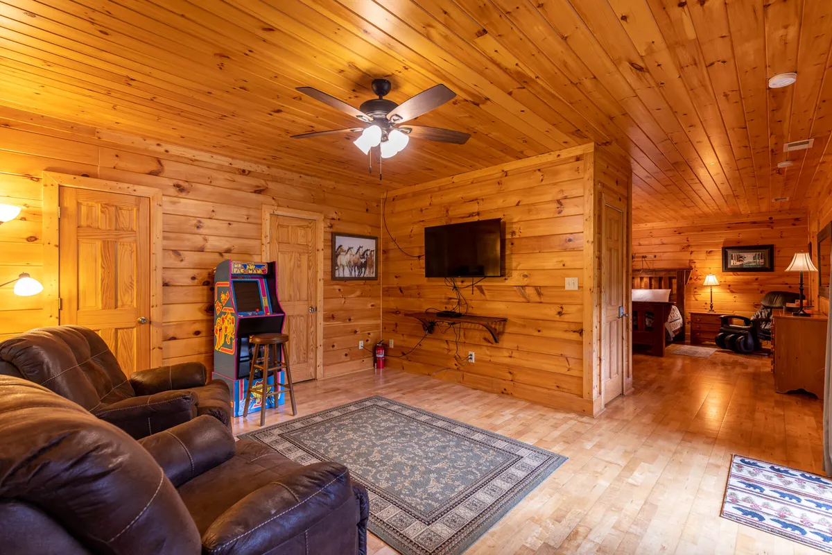 A casual corner featuring leather chairs, a retro arcade game, a television, and rustic wooden walls. The scene hints at both relaxing movie nights and playful game tournaments, blending nostalgia and fun in a cozy mountain setting.