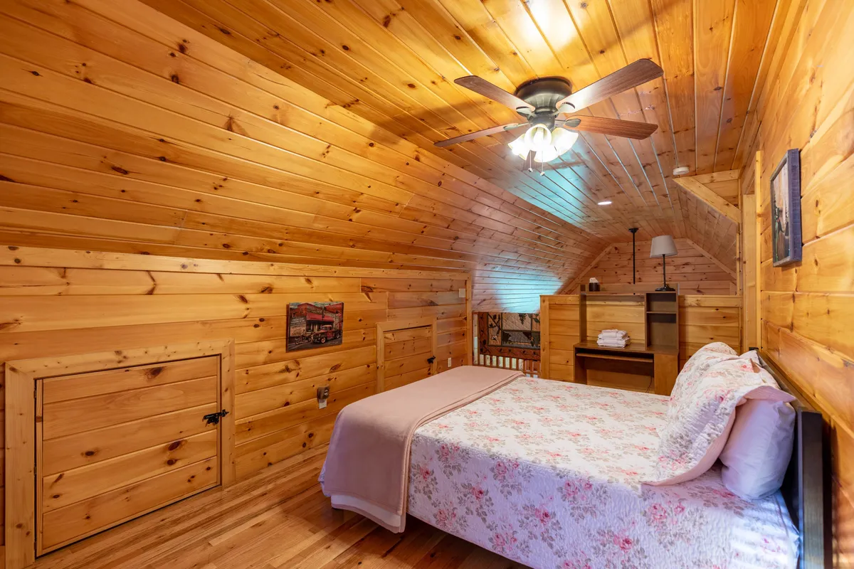 This image features a warmly lit bedroom with a floral bedspread, wooden ceiling, ceiling fan, and rustic wooden furnishings. The ambiance is tranquil and private, suggesting a master suite or private retreat for adults to unwind and relax.