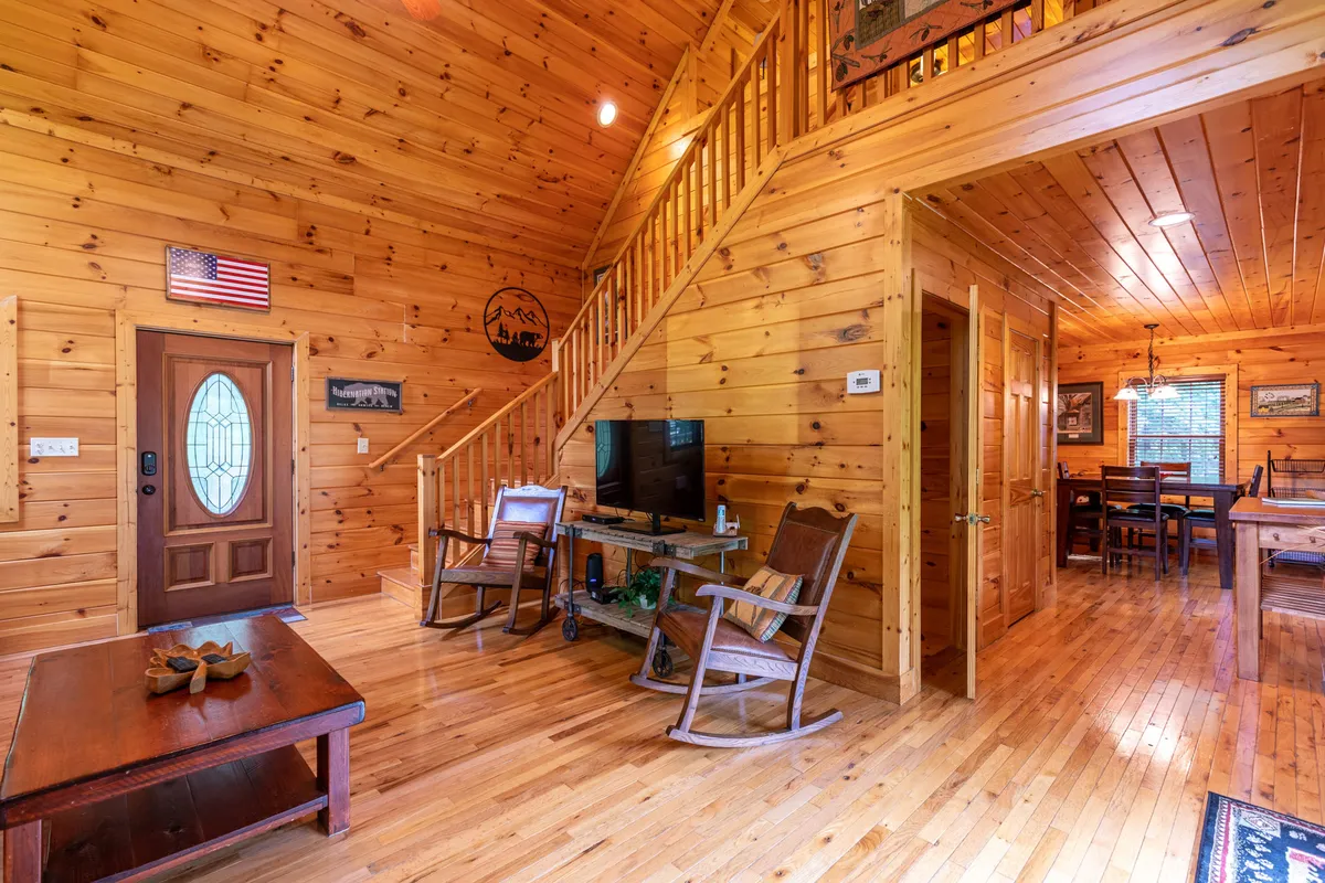 A welcoming area near the front door with a wooden staircase, rocking chairs, views into the dining area, and a television. The space blends elements of relaxation, socializing, and easy transition to the outdoors—the rocking chairs hint at porch comfort, even if pictured inside.