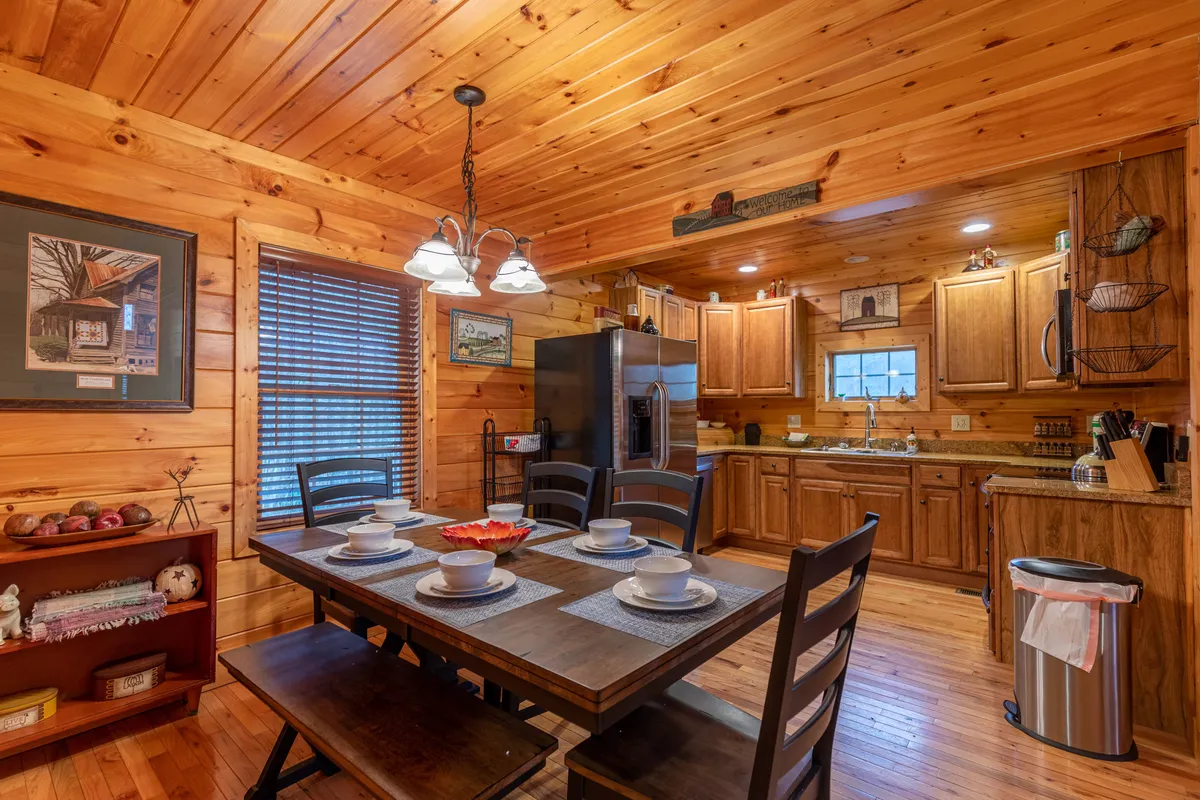 A beautifully set dining table is the focal point, surrounded by modern kitchen appliances and warm wooden cabinetry. The setup invites shared meals, cooking, and entertaining, with decorative art adding a homely touch.