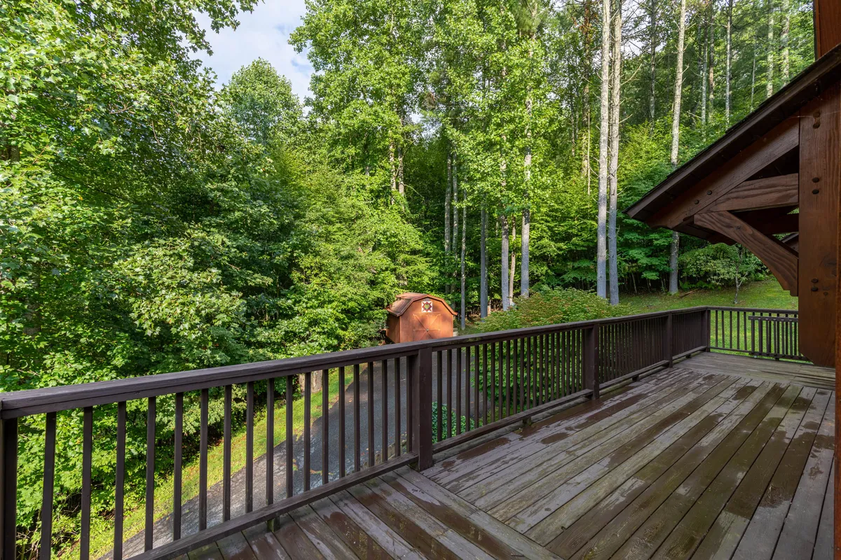 An exterior shot of a wooden deck surrounded by mature trees and a small shed, evoking the feeling of a private, fenced, and secure outdoor area. The lush greenery and open space suggest ample room for children and pets to play.